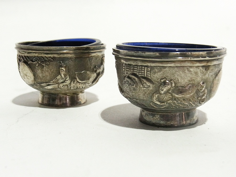 A pair of Chinese silver-coloured metal salts of pedestal form with repousse frieze decoration of