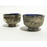 A pair of Chinese silver-coloured metal salts of pedestal form with repousse frieze decoration of