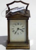 Brass carriage clock with shaped hinged handle above arched pediment over dentil cornice to fluted