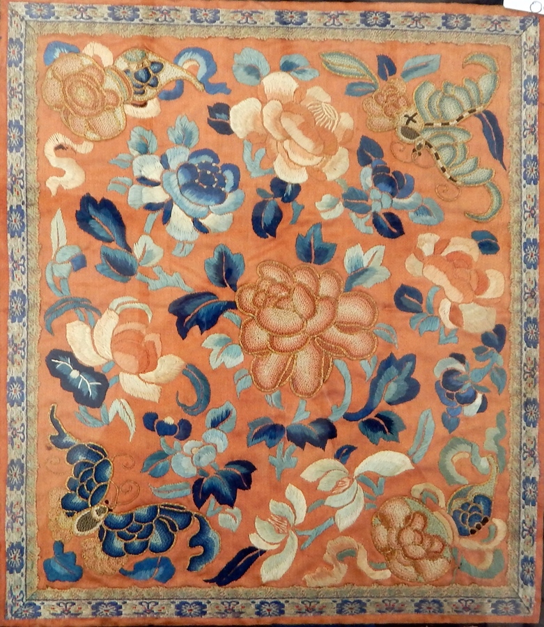 A framed piece of oriental embroidery showing blue and apricot flowers on an apricot ground with a