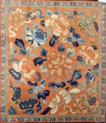 A framed piece of oriental embroidery showing blue and apricot flowers on an apricot ground with a