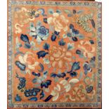 A framed piece of oriental embroidery showing blue and apricot flowers on an apricot ground with a