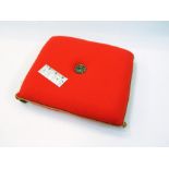 A Prince of Wales Investiture pillow in orange wool trimmed with gold braid and a metal insignia