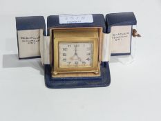 Zenith gilt metal cased travelling clock of angular form on bun feet mounted in blue leather case,