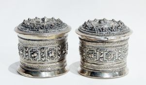 A pair of Eastern silver circular lidded pots with oval repousse decoration,