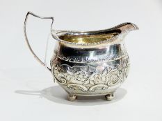 George III silver cream jug with gadrooned border and floral repousse design, raised on ball feet,