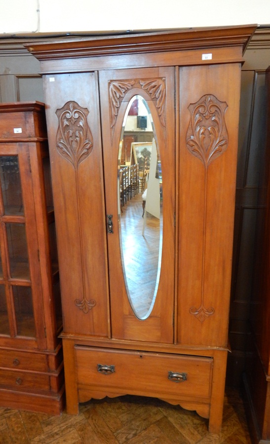 A late Victorian satin walnut wardrobe with oval mirror door, enclosing hanging space, drawer below,