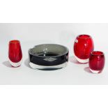 A grey glass ashtray and three red cylindrical vases