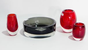 A grey glass ashtray and three red cylindrical vases