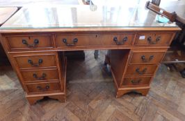 A reproduction yew wood veneer pedestal desk with inset leather writing surface and glass top,