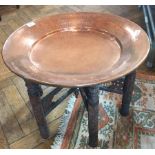 An Eastern folding occasional table with heavy beaten copper circular top on carved supports,