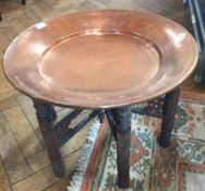 An Eastern folding occasional table with heavy beaten copper circular top on carved supports,