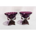 A pair of amethyst glass bowls on bronze-effect moulded stands, each of three scroll arms,