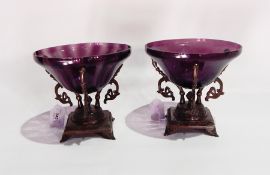 A pair of amethyst glass bowls on bronze-effect moulded stands, each of three scroll arms,