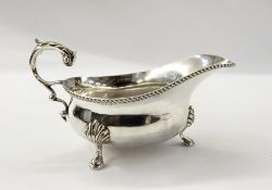 George VI silver gravy boat with foliate scroll handle, gadrooned border, on shell pad feet,