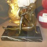 A bronze cast of a seated semi-nude female on a marble base