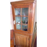 An antique pine corner cabinet fitted glazed panel door above further panelled door enclosing