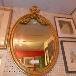 A C19th wall mirror the original oval bevelled plate within carved giltwood frame with carved