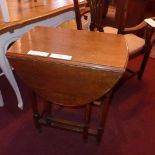 An Edwardian oak drop flap table with twin oval flaps and raised on turned stretchered supports