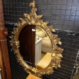 An ornate gilted oval wall hanging mirror