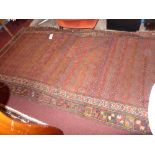 A hand made antique Persian carpet decorated with a repeating motif on a red field surrounded by two