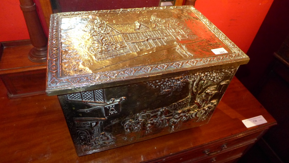 A brass clad log bin with landscape scenes in relief