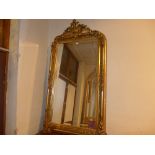 A wall mirror with bevelled arched plate within ornate gilt frame with leafy surmount