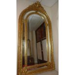 A wall mirror of large size with arched bevelled plate with ornately carved divisional gilt frame