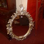 An oval wall mirror within ornate silvered leafy frame