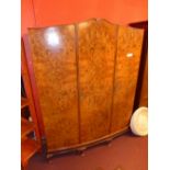 A Queen Anne style burr walnut triple wardrobe fitted three panel doors enclosing hanging space on
