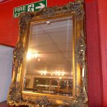 A wall mirror the rectangular bevelled plate within ornate heavy gilt frame