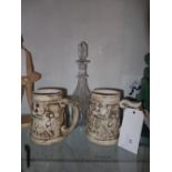 A Victorian cut glass decanter with etched detail and a pair of Continental pottery tankards (3)