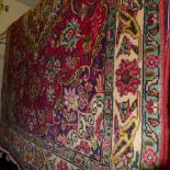 A Persian style carpet the red ground with floral motifs and within a blue and beige border