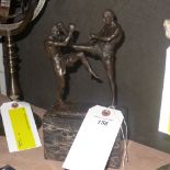 A bronzed figure of kick boxers on a marble stand
