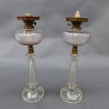 A pair of Victorian clear glass oil lamps, the squat circular reservoir on faceted cut column and