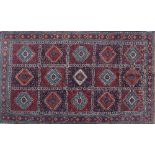 A hand woven Caucasian carpet, the rouge and indigo panelled field with alternating red and blue