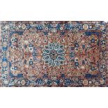 A hand woven Nahavand Persian rug, madder ground with blue floral medallion and border. Width 147