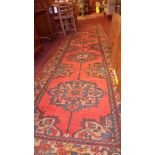 A Persian hand knotted Heriz runner the red field having fine central medallions with geometric