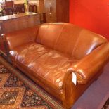 A contemporary designer two seater sofa upholstered in tan leather raised on bun feet