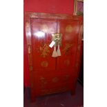 A Chinese red lacquered marriage cabinet having gilded panel doors enclosing fitted drawers