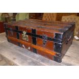 An iron bound stained pine travelling trunk having twin leather carry handles and castors to base