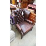 A faux brown leather wing chair with buttoned back above cushioned seat on square section supports