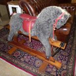 A Pegasus Toys rocking horse, with a grey plush body and red leather saddle and tack, on a natural