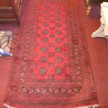 An Afghan hand made rug decorated with repeated motifs on a red field surrounded by four running