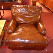 A Howard style armchair upholstered in tan hide leather raised on turned mahogany supports and