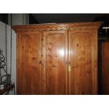 An early C20th pine triple wardrobe with panel doors over four drawers on plinth base