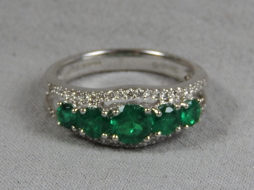 A white metal green five stone ring encompassed by diamond chips.