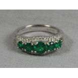 A white metal green five stone ring encompassed by diamond chips.