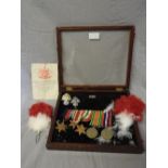 A glazed box of military objects, including spire fine replica medals, two badges and two feather