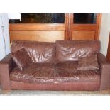 A pair of distressed brown leather two seater sofas with four matching cushions (2) 210cm(w) 95cm(d)